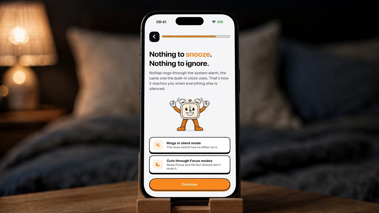 An iPhone on a stand on a nightstand at night showing the NoNap onboarding screen reading Nothing to snooze, nothing to ignore, with two rows explaining that the alarm rings in silent mode and cuts through Focus modes