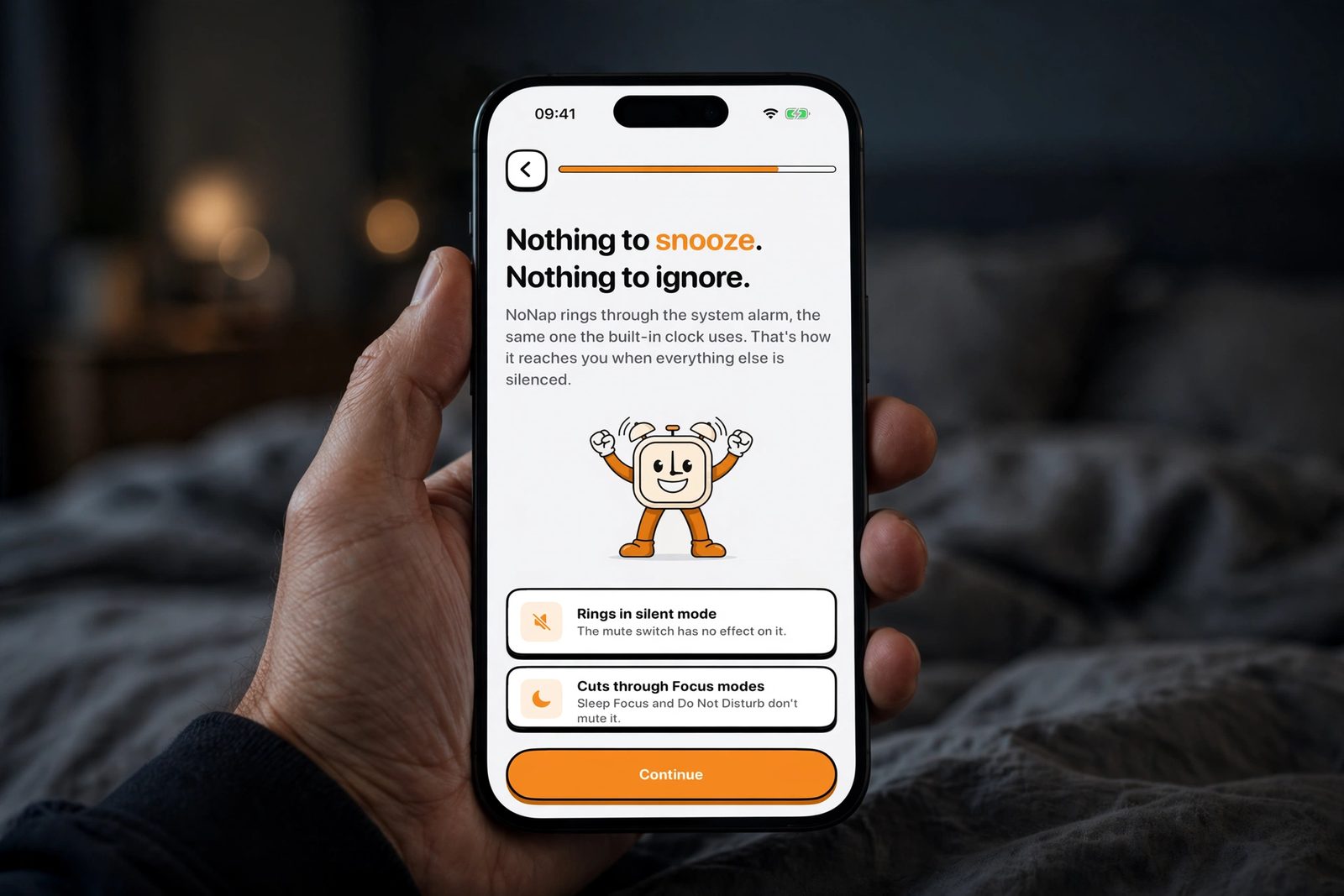 A hand holding an iPhone in a dim bedroom, showing NoNap's onboarding screen explaining that the alarm rings in silent mode and cuts through Focus modes