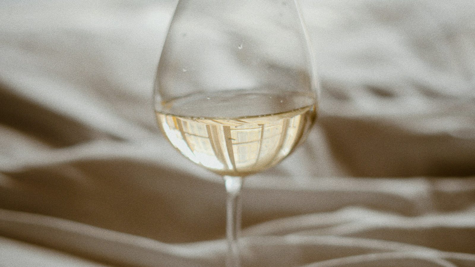 A glass of wine backlit on rumpled bed sheets at night