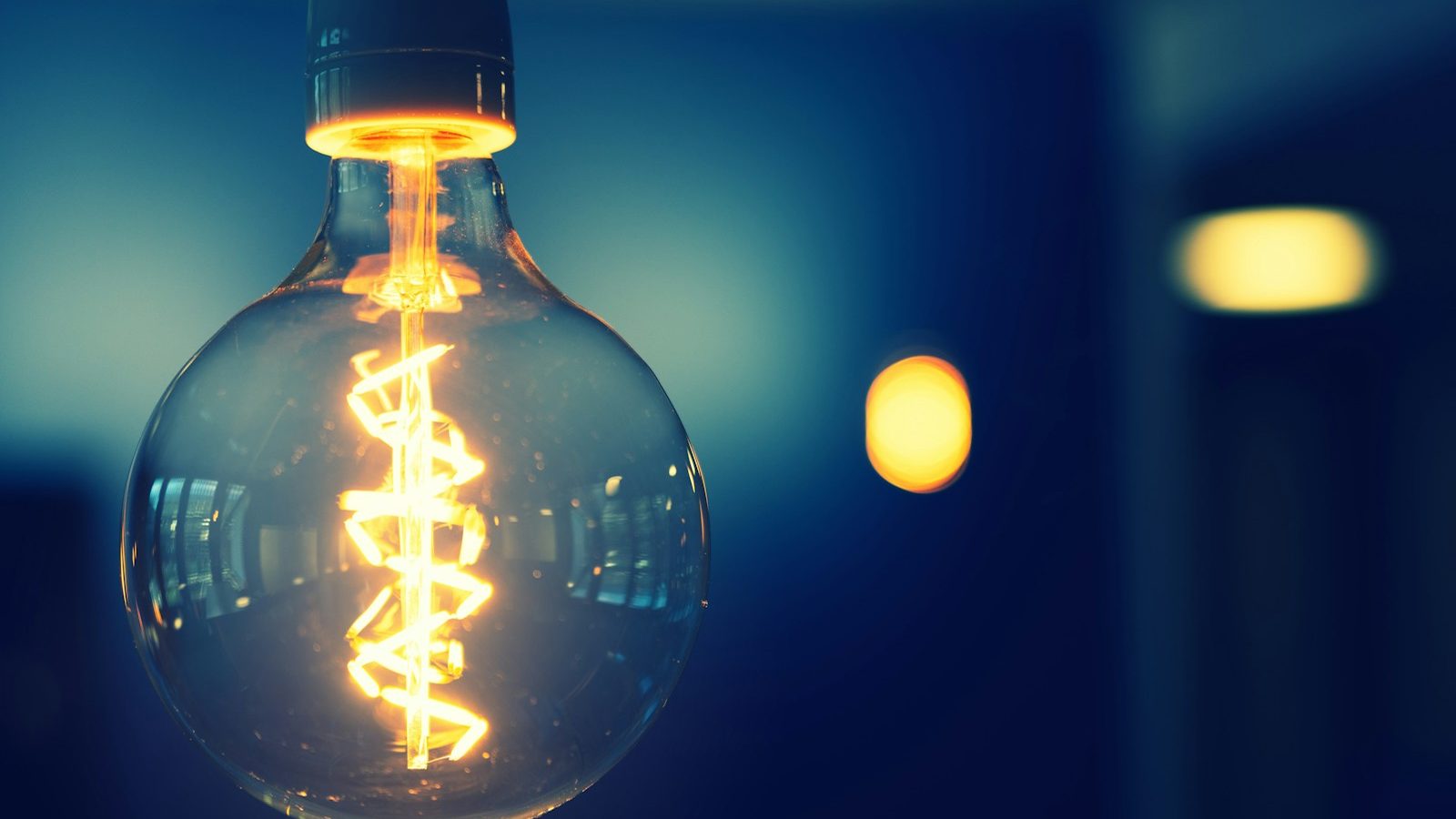 Close-up of a glowing warm light bulb filament against a dark blue background with bokeh lights