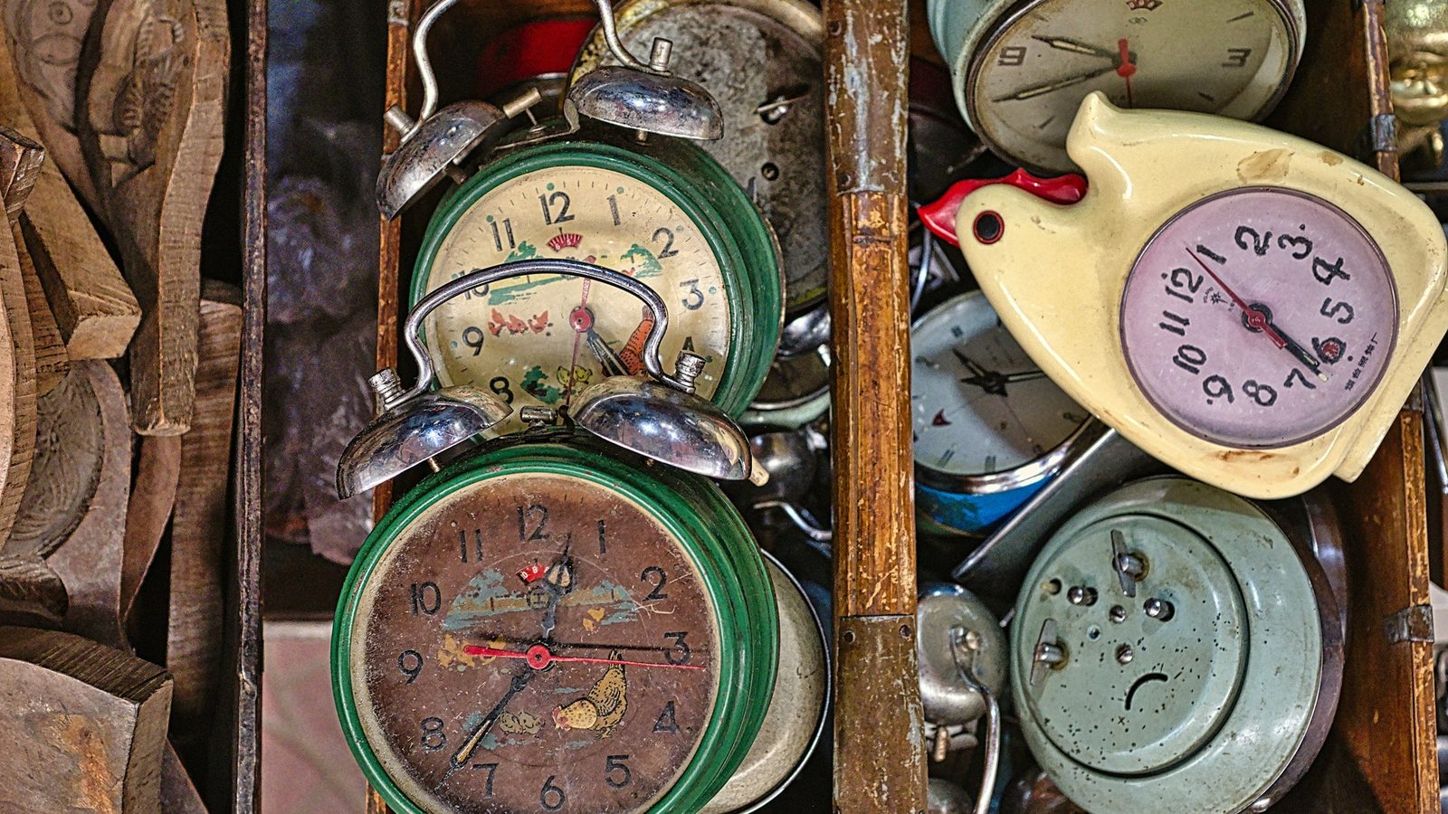 A wooden crate crammed with mismatched vintage twin-bell alarm clocks at a flea market