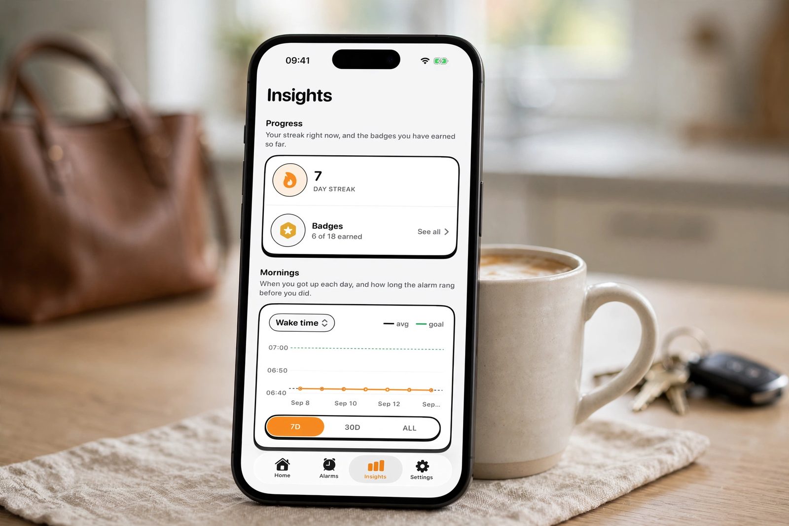An iPhone propped against a coffee mug on a kitchen counter, showing NoNap's insights dashboard with streaks and wake-up time consistency over recent weeks