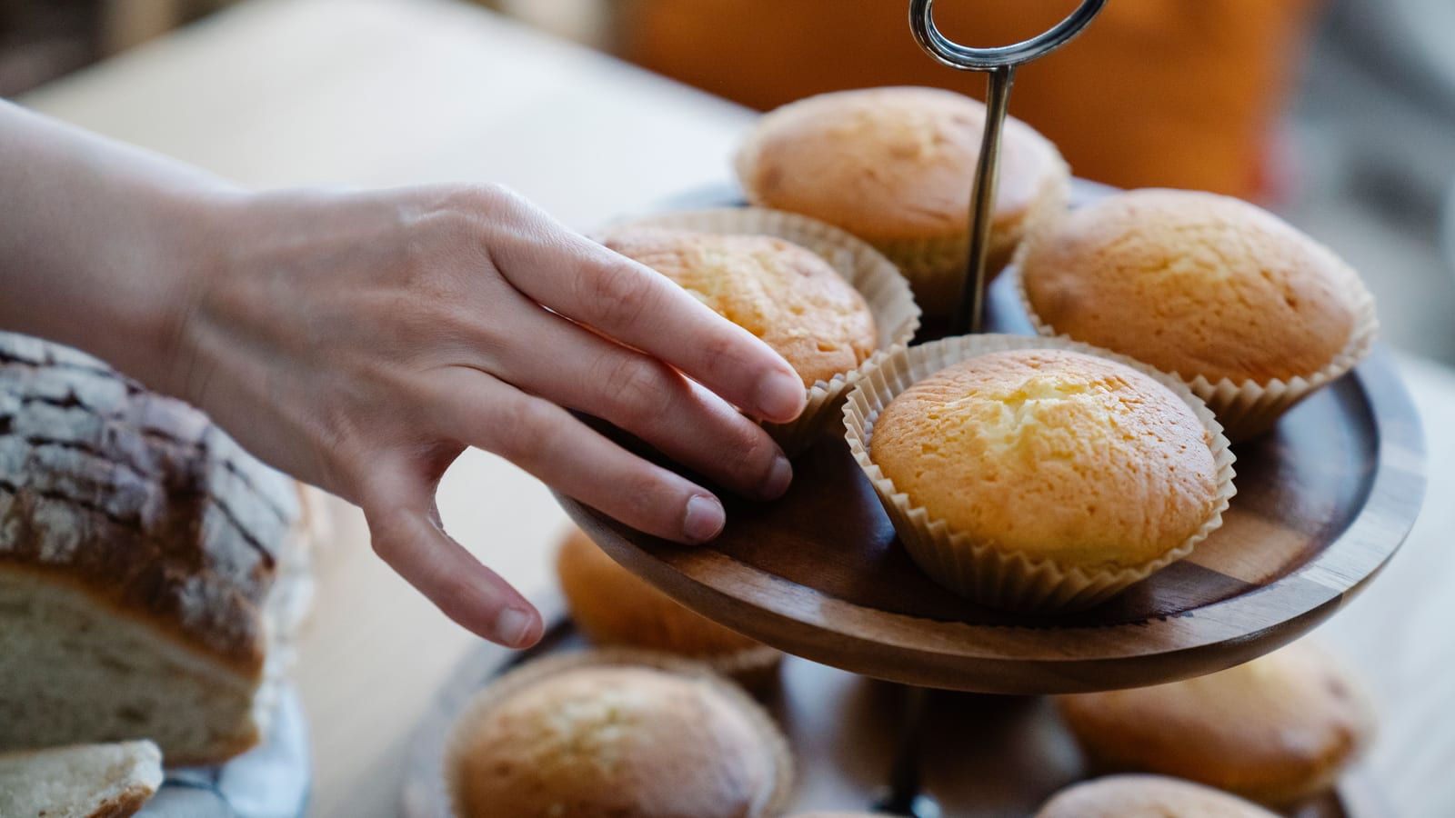A hand reaching for a cupcake from a tiered stand of freshly baked muffins